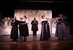 Theatre still photo of a group of people singing wearing Victorian clothing.